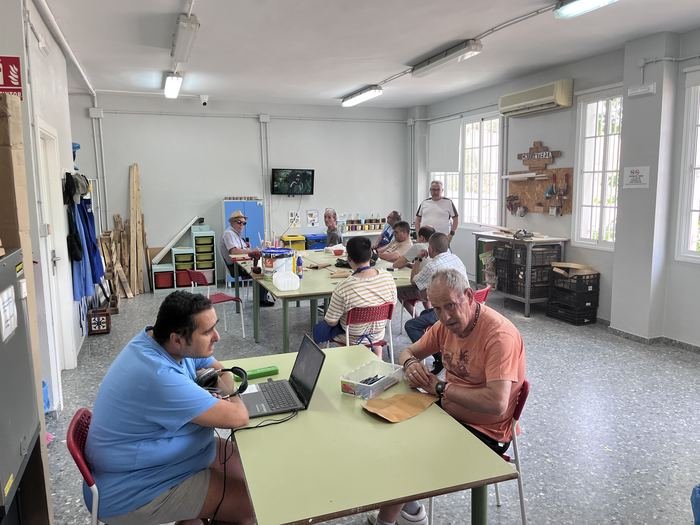 Sala de taller con personas trabajando en mesas y materiales al fondo