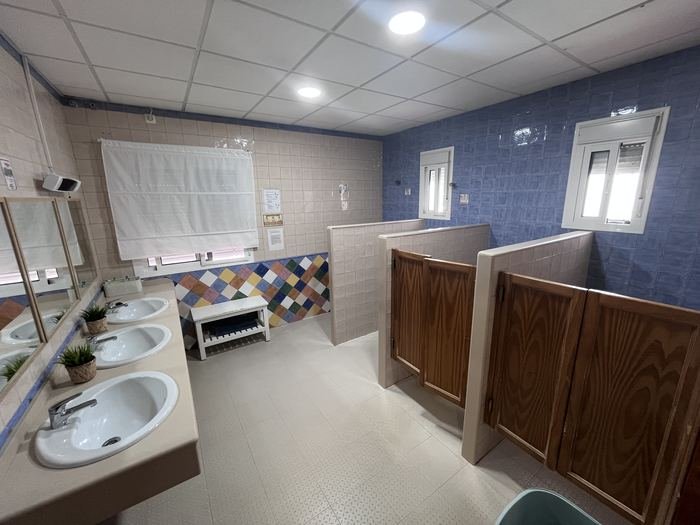 Baño de la residencia con lavabos, cabinas de madera y paredes de azulejo