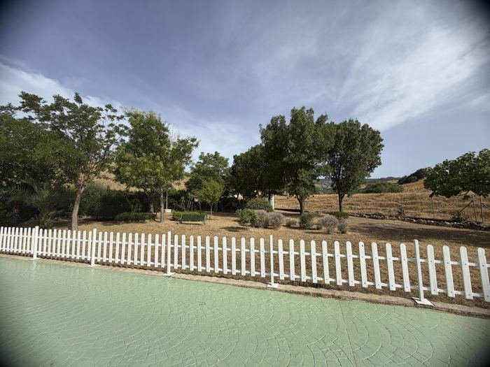 Zona ajardinada con vallado blanco y árboles